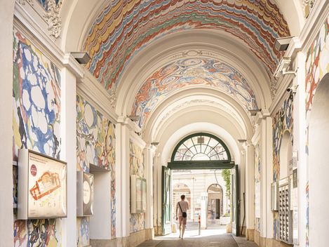 View through an arched passage decorated with colorful marble patterns with an open gate and a person in the background