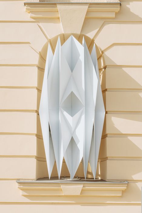 Architectural detail with vertically arranged pointed white panels in a niche of a light-colored facade
