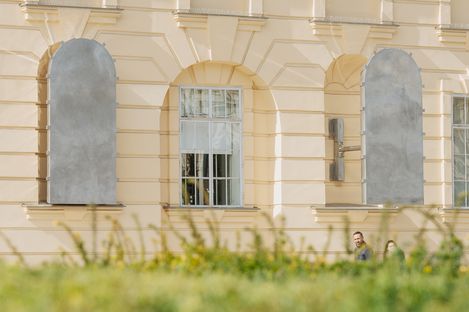 Facade of a historic building with two silver art installations in front of window niches and an open window in the centre