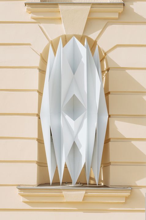 Architectural detail with vertically arranged pointed white panels in a niche of a light-colored facade
