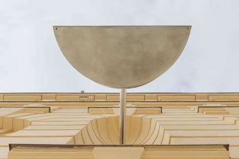 Half-round metal mirror on a pole in front of a yellowish facade with rectangular windows