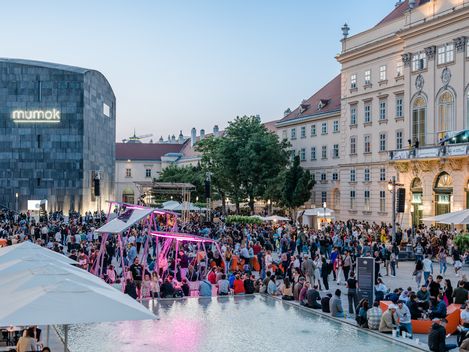 Große Menschenmenge bei einem Sommerfest vor dem mumok-Museum mit moderner und historischer Architektur im Hintergrund
