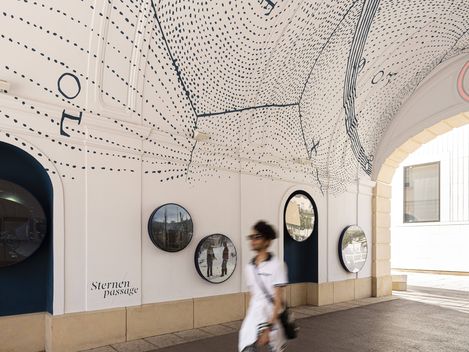 Ceiling of a passageway with a black-and-white line drawing depicting constellations and dots, round images on the wall below, and a person walking past