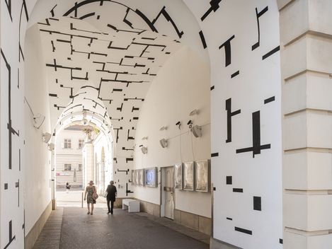 Arched passageway with white walls decorated with black geometric line patterns, two people walking through