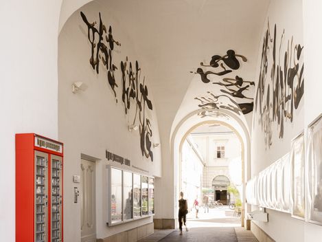 Arched passage with white vaulted ceiling and black abstract wall paintings and a red mailbox on the left wall