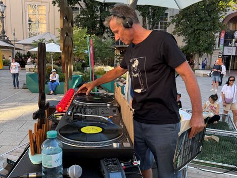 Man wearing headphones stands at outdoor DJ booth holding a vinyl record