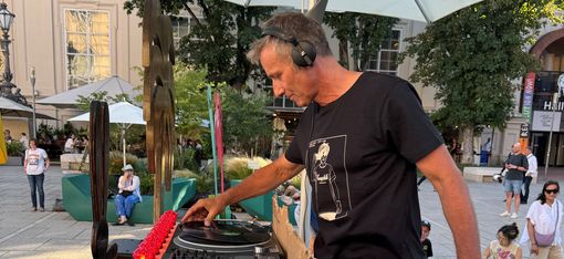 Mann mit Kopfhörern steht an DJ-Pult im Freien und hält eine Schallplatte in der Hand