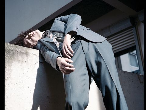 Person leaning against a concrete wall with closed eyes and head tilted back wearing a suit
