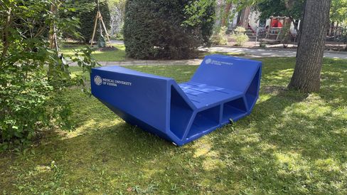 Blaue Enzos mit Branding der Medizinischen Universität Wien stehen auf einer Wiese zwischen Bäumen auf dem Campusgelände.