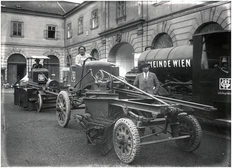 Historisches Schwarz-weiß-Foto mit zwei landwirtschaftlichen Maschinen und einem Tankwagen mit der Aufschrift 'GEMEINDE WIEN' in einem Innenhof mit Arkaden.