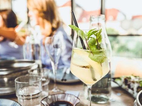 Frisches Getränk garniert mit Minze und Strohhalm in einem Weinglaß auf einem befüllten Tisch.