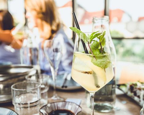 Frisches Getränk garniert mit Minze und Strohhalm in einem Weinglaß auf einem befüllten Tisch.