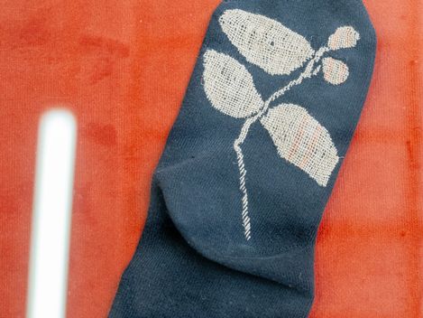 Ein dunkelblauer Socke mit einem weißen Blatt- und Beerenmuster liegt auf einem roten Untergrund