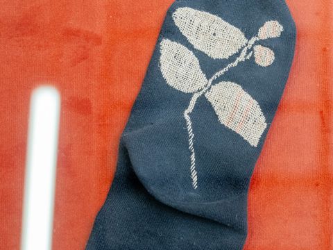 Ein dunkelblauer Socke mit einem weißen Blatt- und Beerenmuster liegt auf einem roten Untergrund