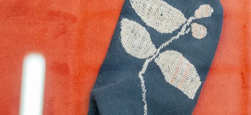 Ein dunkelblauer Socke mit einem weißen Blatt- und Beerenmuster liegt auf einem roten Untergrund