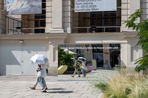 Spiegel mit der Aufschrift 'THIS IS WHAT PEOPLE LIVING IN PEACE LOOK LIKE' vor einem historischen Gebäude mit Menschen, die daran vorbeigehen, und einer weißen Sonnenschirmattrappe.