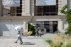 Spiegelwand mit der Aufschrift 'THIS IS WHAT PEOPLE LIVING IN PEACE LOOK LIKE' vor einem historischen Gebäude, zwei Personen gehen vorbei, eine mit weißem Regenschirm