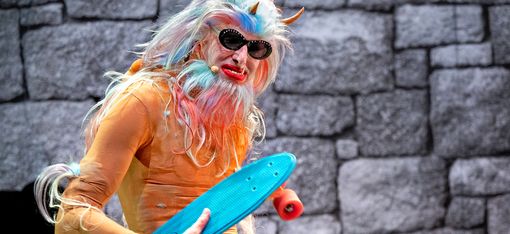Ein Monster mit drei Hörnern, Sonnenbrille, verlängertem Eckzahn und einem Skateboard in der Hand schaut direkt in die Kamera.