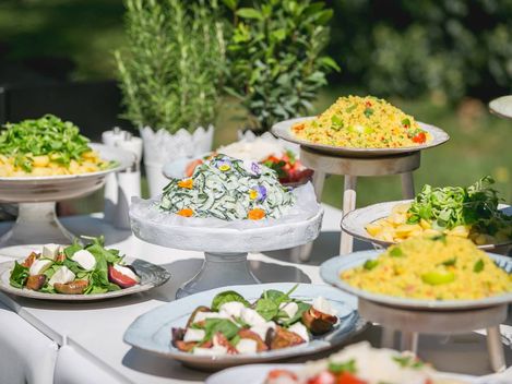 Ein Buffettisch mit einer Vielzahl von Speisen, darunter Salate, Fleischgerichte und Desserts, lädt die Gäste dazu ein, sich selbst zu bedienen.