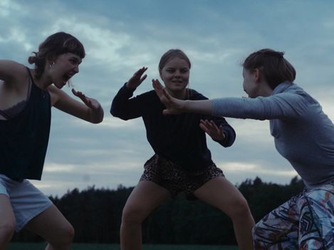 Three young women in athletic clothing in fighting stances outdoors under a cloudy sky