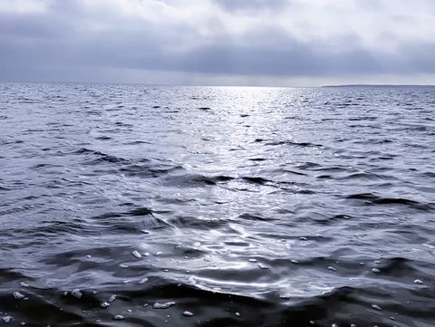 The film still shows dark water stretching as far as the horizon; the sky is covered with dark clouds.