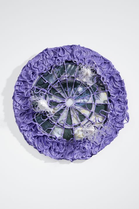 Round object with a central hole surrounded by a purple textured ruffled edge and a web of threads partially covered with white fibers