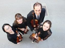 Four people stand in a circle holding string instruments.