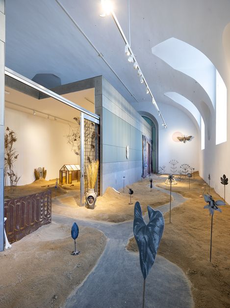 Exhibition room with sand-covered floor, metal plants and decorative elements