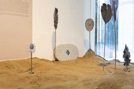 Exhibition room with sand-covered floor, metal plants and decorative elements