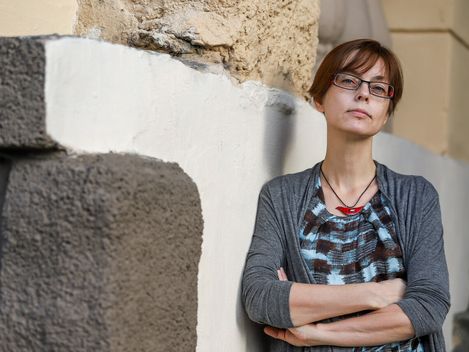 Person with crossed arms leaning against a wall made of rough stone and plaster.