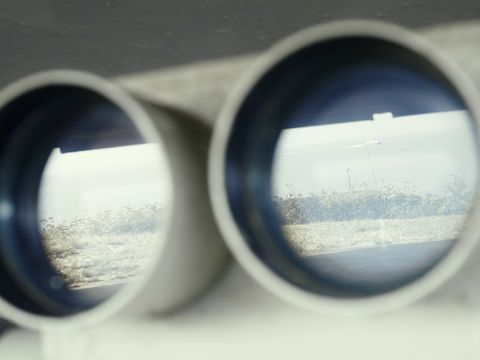 A coastal landscape is reflected in a pair of binoculars.