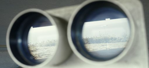 A coastal landscape is reflected in a pair of binoculars.