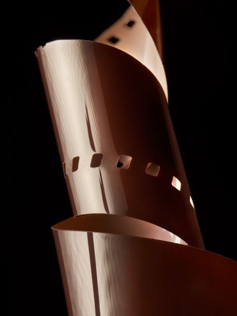 Close-up of a film strip curled into a spiral with square perforations against a black background.