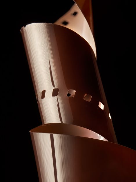 Close-up of a film strip curled into a spiral with square perforations against a black background.