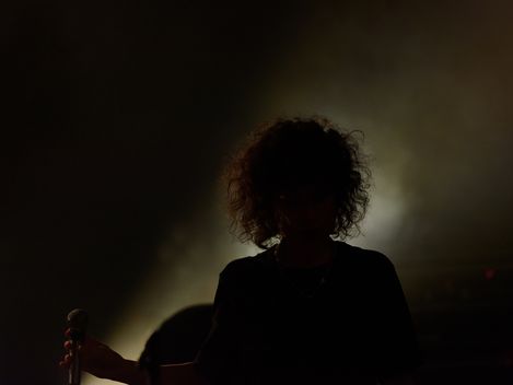Silhouette of a person with curly hair holding a microphone against bright backlight.