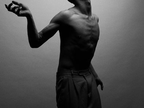 Shirtless man with head tilted upward and right arm raised against a plain background.