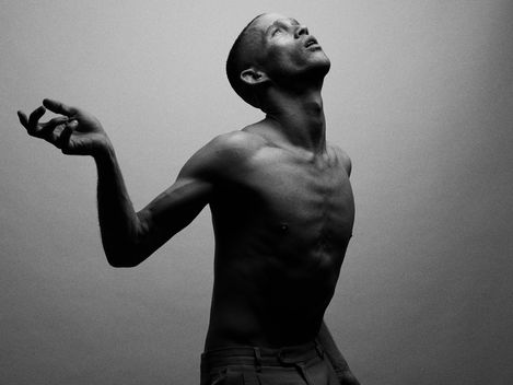 Shirtless man with head tilted upward and right arm raised against a plain background.