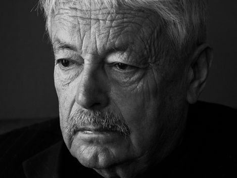 Portrait of a person with short, slightly wavy hair and visible ear against a dark background.