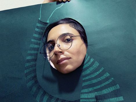 Portrait of a woman wearing round glasses, holding a graphic paper artwork with a neck motif around her face.