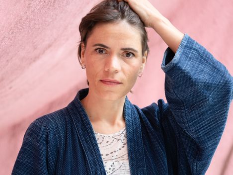 Porträt einer Frau mit kurzem Haar vor rosafarbenem Hintergrund, eine Hand im Haar.