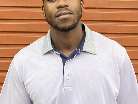 Mann mit weißem Poloshirt vor einer orangefarbenen Wand mit horizontalen Linien.