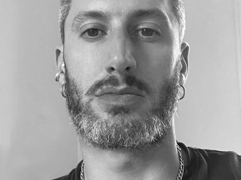 Portrait of a man with short hair, earrings, and a chain necklace wearing a t-shirt.
