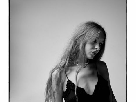 Black-and-white portrait of a woman with long hair wearing a black sleeveless dress against a plain background