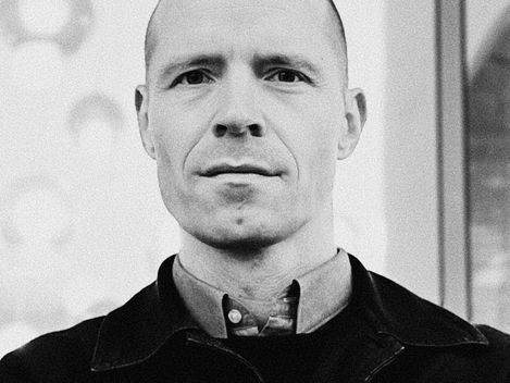 Black-and-white portrait of a man with short hair wearing a shirt and jacket against a blurred background.