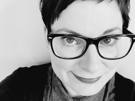 Person with short hair, glasses, and button-collar shirt in a black-and-white close-up.