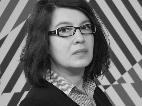 Woman with shoulder-length hair and glasses in front of a geometric patterned wall