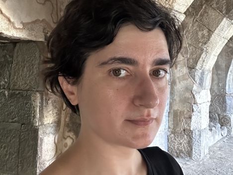 Person with short dark hair and black top in front of a stone arch wall.