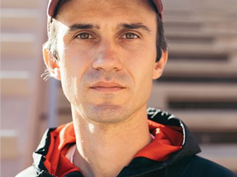Person wearing a baseball cap and jacket standing in front of stairs with face blurred.