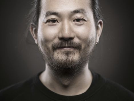 Portrait of a man with tied-back hair and beard against a dark background.