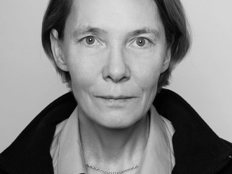 Portrait of a woman with short hair wearing a shirt and jacket against a neutral background